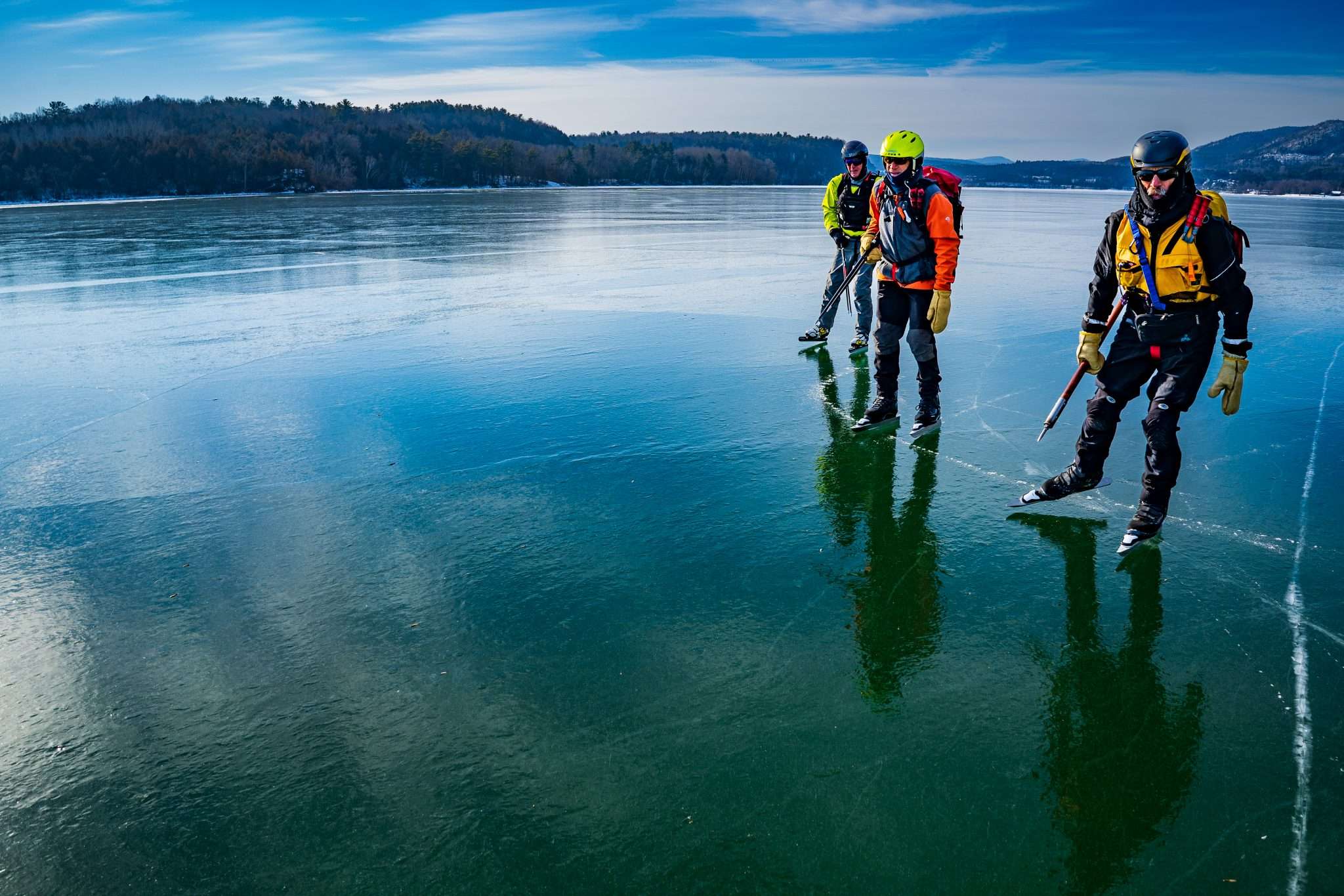 Dan Spada, John Rosenthal, and Dave Phillips are pictured skating across a blue and icy Lake Champlain off Fort Ticonderoga in helmets, vests and other gear.