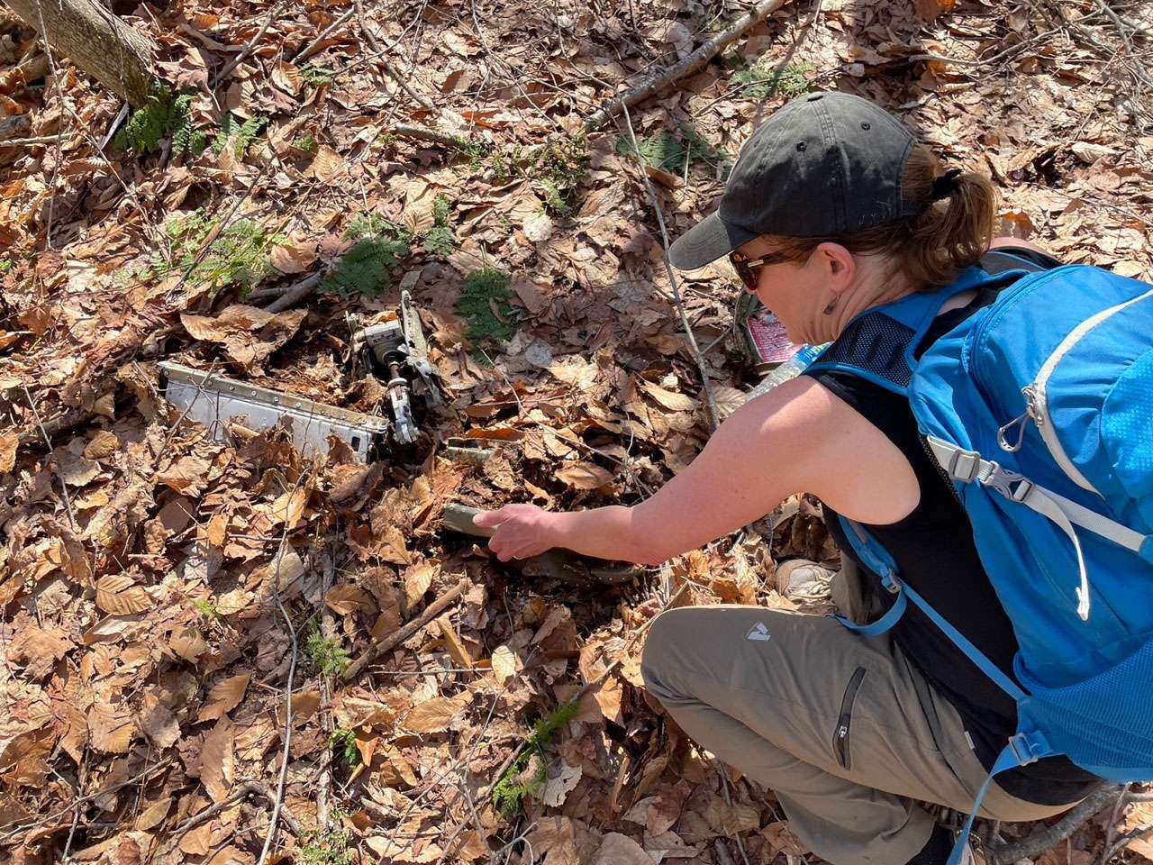 A woman with blue backpack digging through leaves on the ground