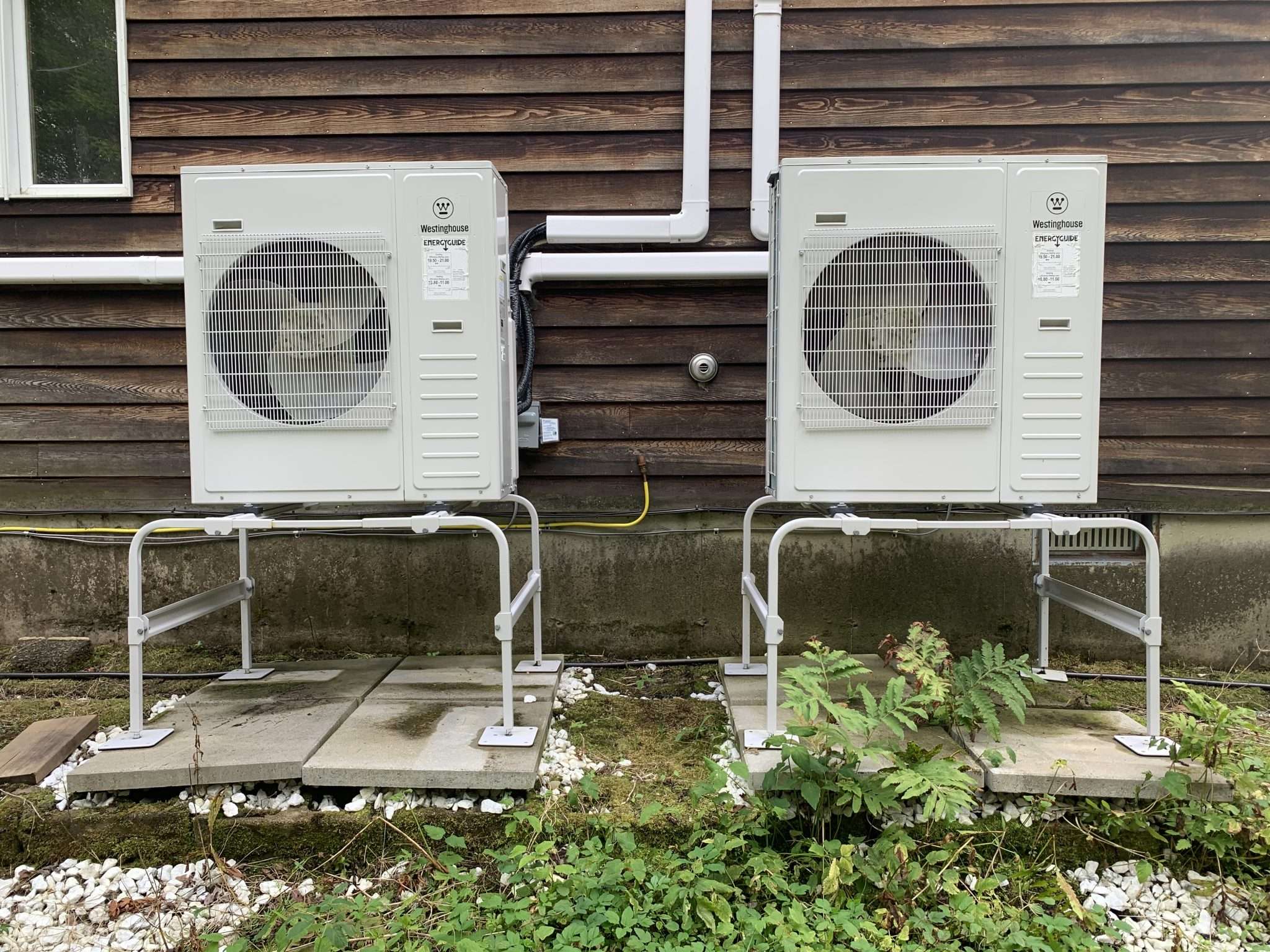 Two heat pumps installed on the side of a house.