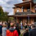 group of people standing in front of a brown house