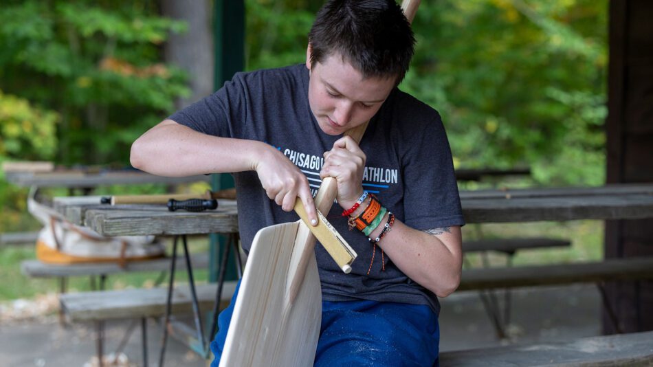 a young man carving a paddle