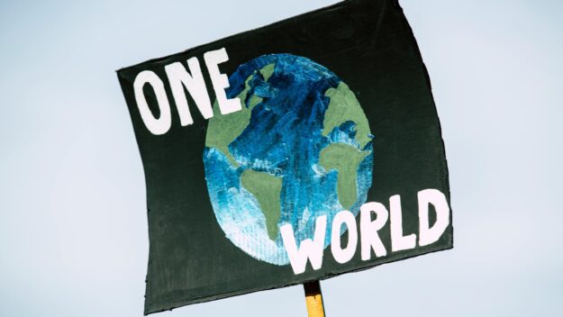 A sign says "one world" over a painting of the Earth