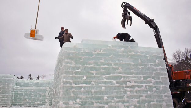 a cran lifts large block of ice to the top of the ice palace wall