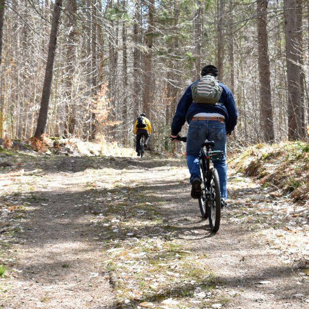 two men on bikes riding up a hill in Wanakena