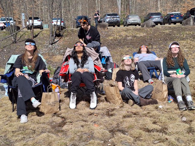 young people in lawn chairs wearing eclipse glasses