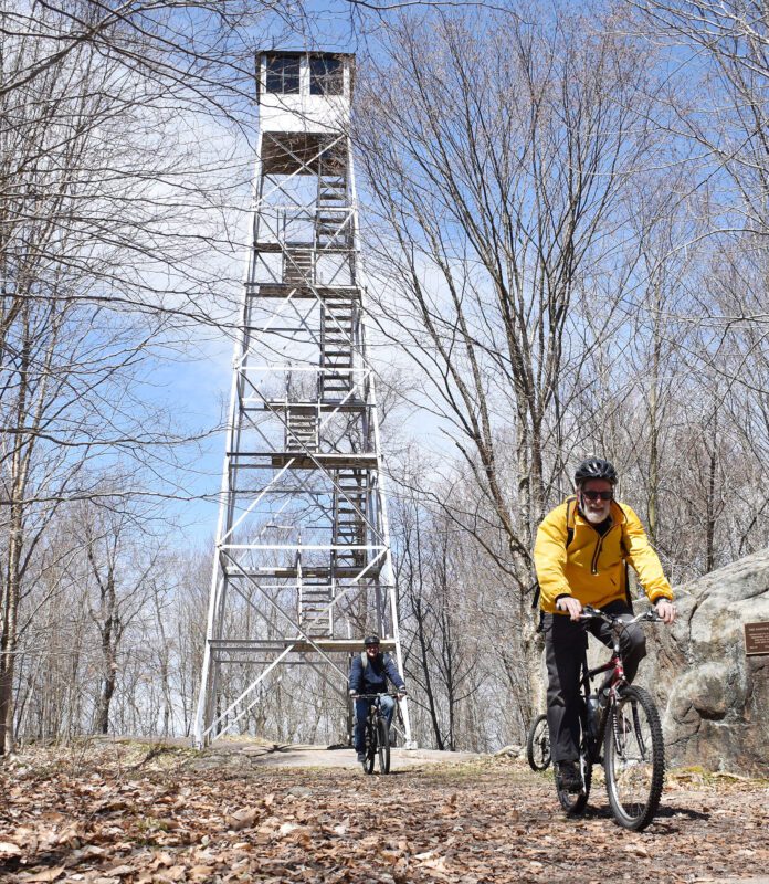 man riding bike with Wanakena fire tower in the background