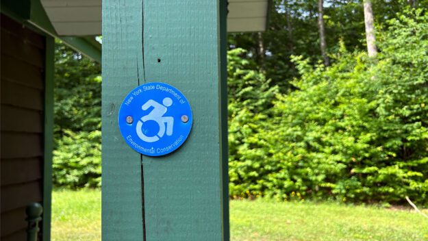 Green wooden pillar of a campsite bathroom with a wheelchair-accessible medallion on it.