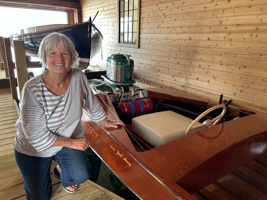 Woman kneels next to small wooden racing boat.