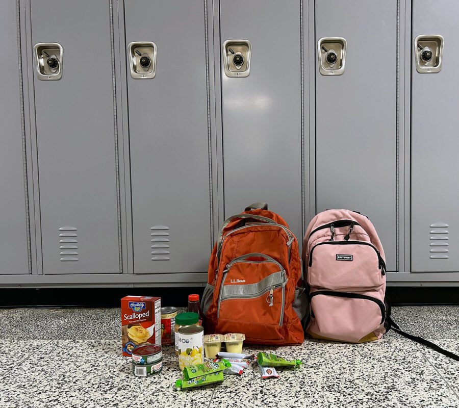 Two backpacks sit in front of a row of lockers, with some non-perishable food beside them.
