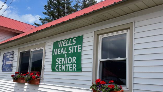 Outside of a white building with flower boxes and a sign that says "Wells Meal Site and Senior Center".