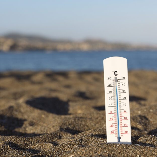 A thermometer showing high temperatures stuck in sand