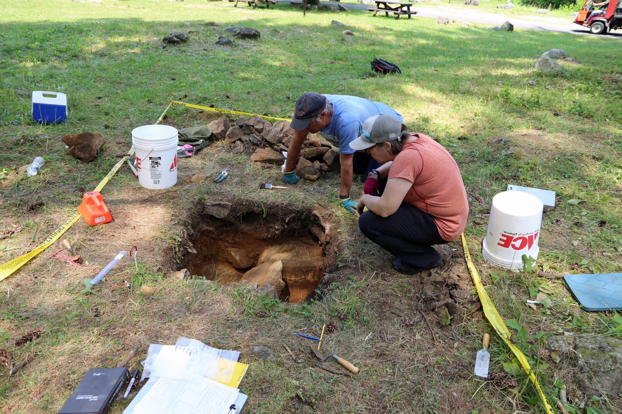 Two people examine an archaeological test pit at the Lake George Battlefield Park