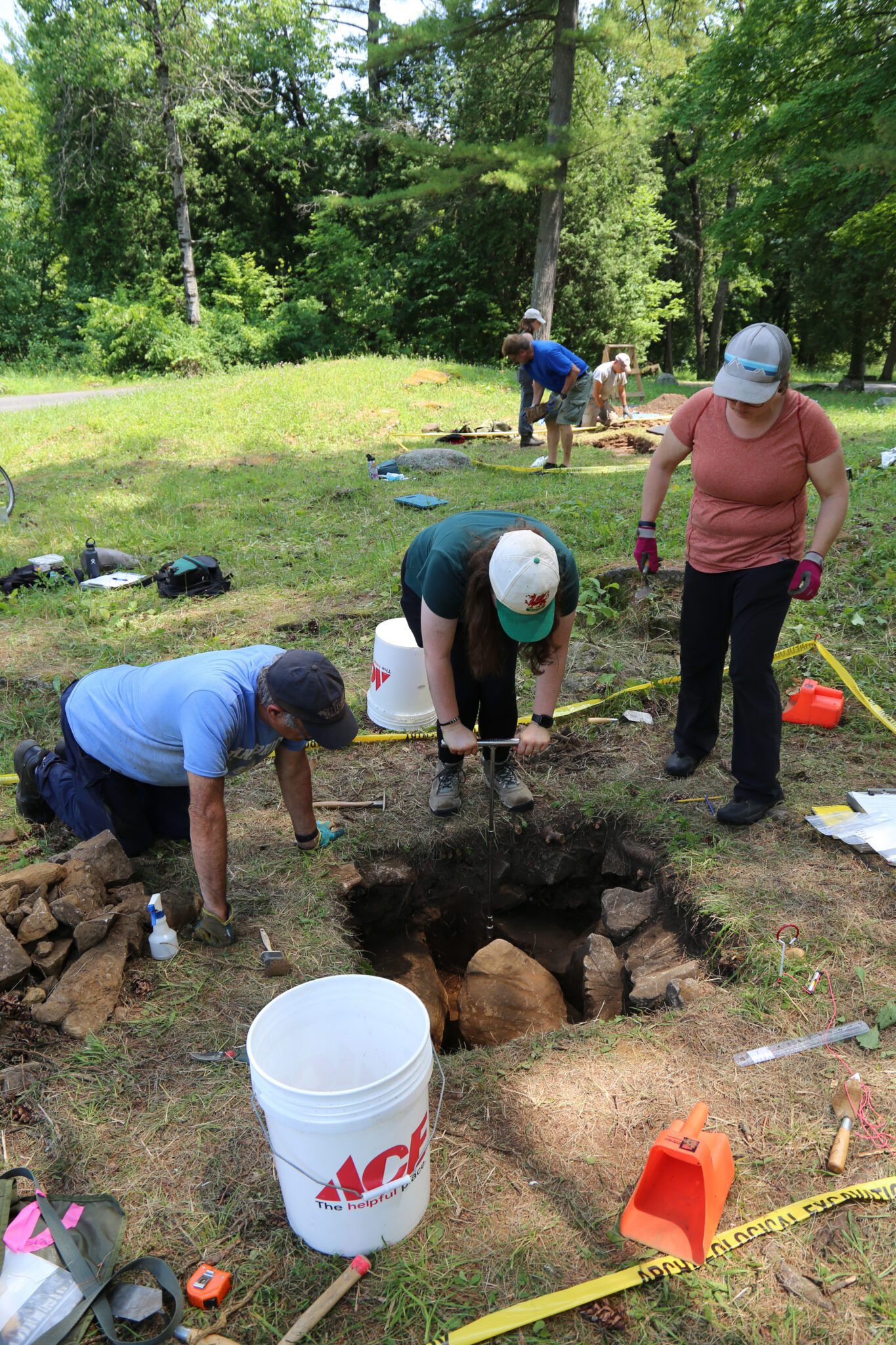 Three people examine an archaeological test pit 