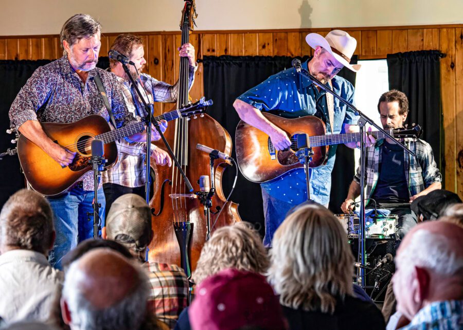 Two men perform on a stage with guitars. One is wearing a cowboy hat.