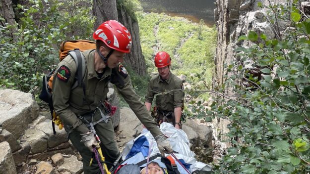 Rangers Charlie Foutch, top and Andrew Lewis, assist an injured hiker down the Trap Dike at Avalanche Lake on Mount Colden in July 2023