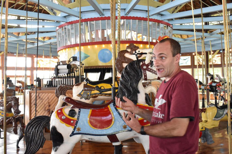 A man speaks in front of a restored carousel.