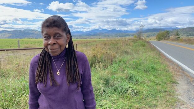 Author Alice Green, wearing purple and standing near green plants at a roadside