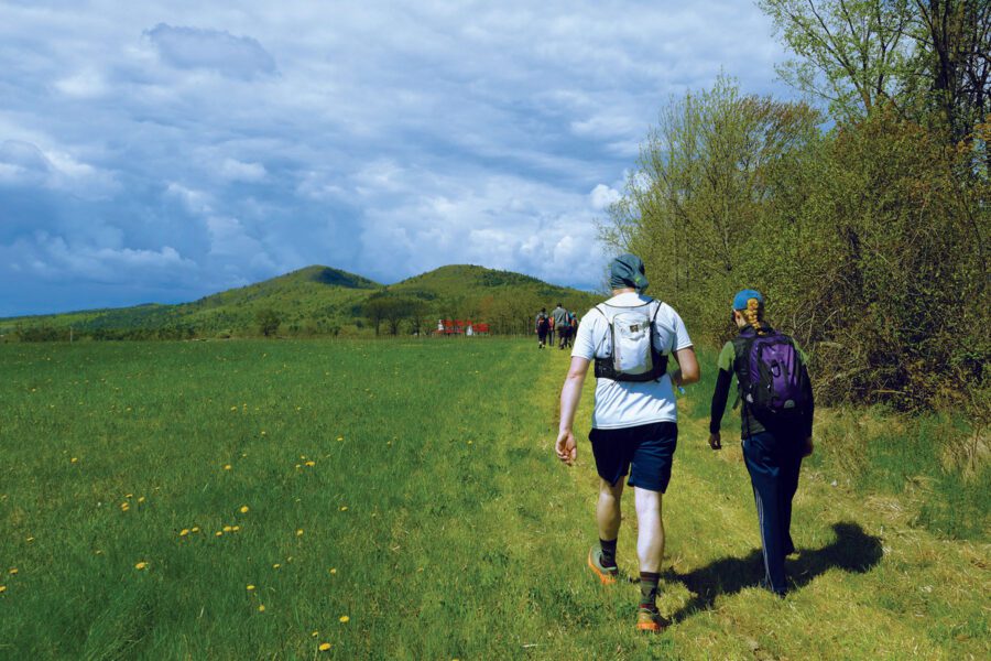 Two hikers in a flat field with mountains ahead