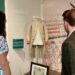 Two museum visitors look at a faded white and pink vintage army uniform.