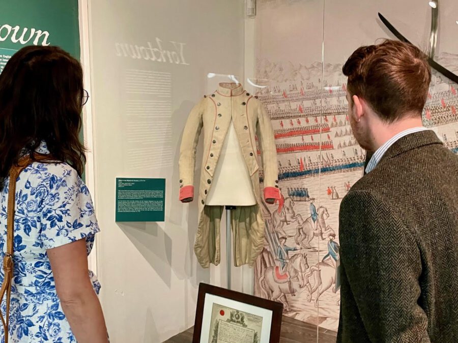 Two museum visitors look at a faded white and pink vintage army uniform.