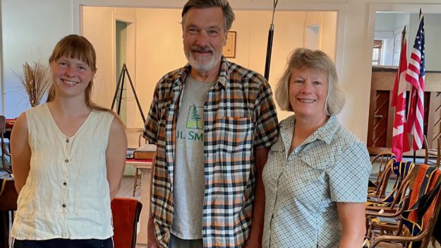 A man in a plaid shirt and two women pose together.