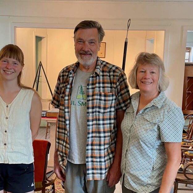 A man in a plaid shirt and two women pose together.