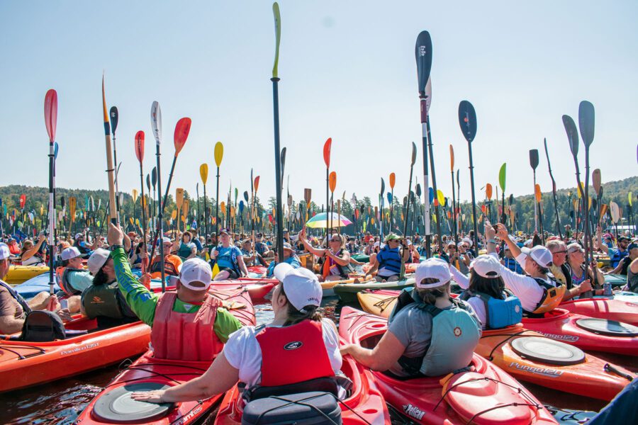 hundreds of paddlers hold their paddles up at one square mile of hope paddling event in inlet