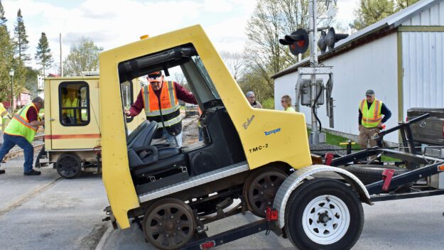 A man in a reflective vest eases a rail car onto the ground off of a lift.