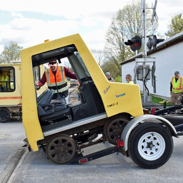 A man in a reflective vest eases a rail car onto the ground off of a lift.