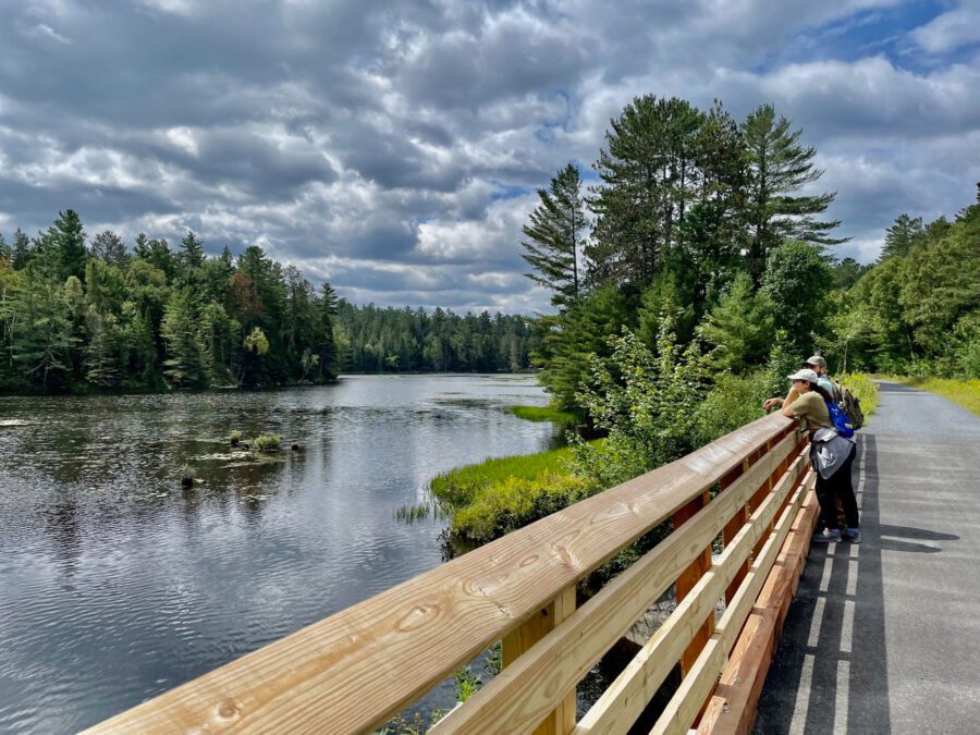 Hikers on the rail trail gaze at the river west of Lake Placid.
