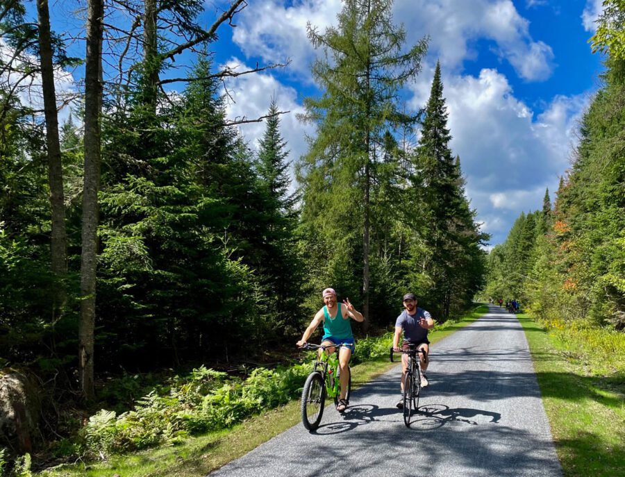 Bike riders smiling and giving a wave outside of Saranac Lake.
